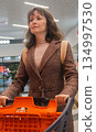 Woman shopping in supermarket. Customer in shopping mall. Brunette woman with shopping cart choosing food. Girl buying goods in market. Shopping expenses. Lifestyle of modern woman.  134997530