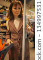 Woman shopping in supermarket. Customer in shopping mall. Brunette woman with shopping cart choosing food. Girl buying goods in market. Shopping expenses. Lifestyle of modern woman.  134997531