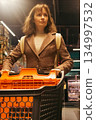 Woman shopping in supermarket. Customer in shopping mall. Brunette woman with shopping cart choosing food. Girl buying goods in market. Shopping expenses. Lifestyle of modern woman.  134997532