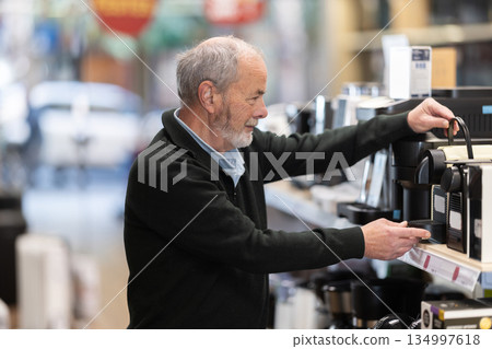 Elderly man chooses coffee machine in hypermarket Elderly man chooses coffee machine in hypermarket 134997618