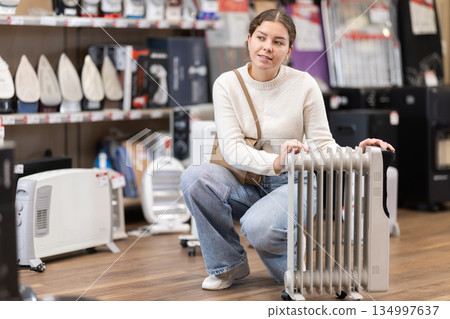 Positive young woman choosing oil heater in hypermarket 134997637