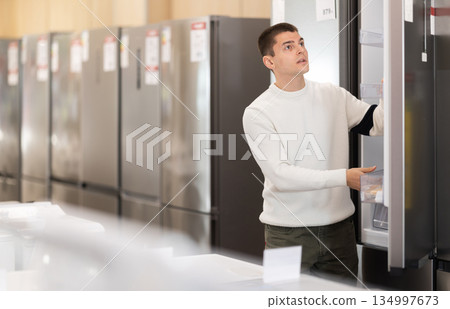 Young man buyer examine fridge in detail before buying Young man buyer examine fridge in detail before buying 134997673