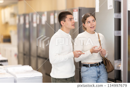 Young couple chooses modern fridge at hypermarket Young couple chooses modern fridge at hypermarket 134997679