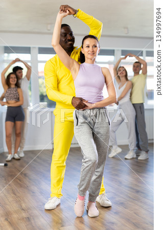 Positive African american man and european woman dancing and training movements Latin dance bachata during group class in choreography studio Positive African american man and european woman dancing and training movements Latin dance bachata during group class in choreography studio 134997694