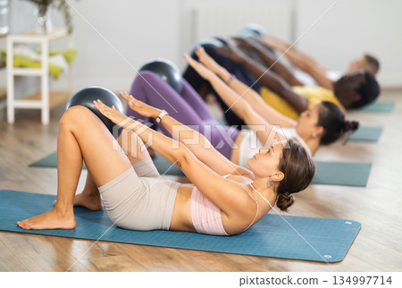 Men and girls hold fitball in their lap, raise and lower torso Men and girls hold fitball in their lap, raise and lower torso 134997714