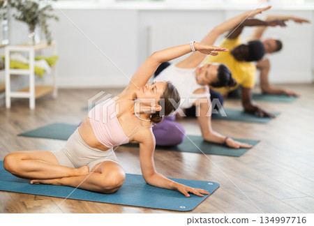 Young girl doing side bend in lotus pose during yoga class Young girl doing side bend in lotus pose during yoga class 134997716