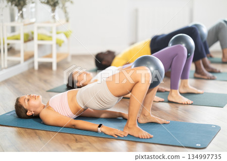 Men and woman diligently perform set of exercises with fitball during training session Men and woman diligently perform set of exercises with fitball during training session 134997735