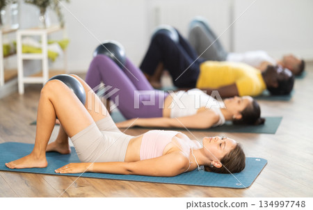 Woman performing glute bridge with ball during group pilates class Woman performing glute bridge with ball during group pilates class 134997748