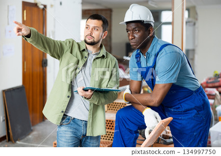 Worker and owner building discuss construction plan inside building under construction 134997750