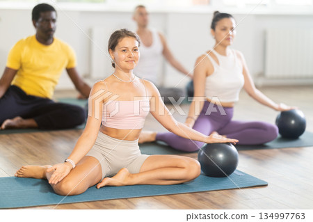 Young woman doing pilates with soft ball in group Young woman doing pilates with soft ball in group 134997763