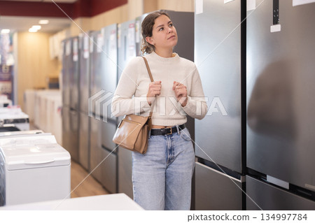 Woman choosing a large refrigerator in a store with appliances 134997784