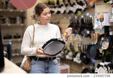 Girl customer inspect product range and selects frying pan 134997786
