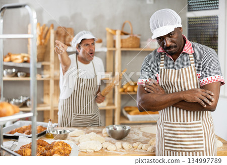 In bakery kitchen, confused African male employee during quarrel with man boss In bakery kitchen, confused African male employee during quarrel with man boss 134997789