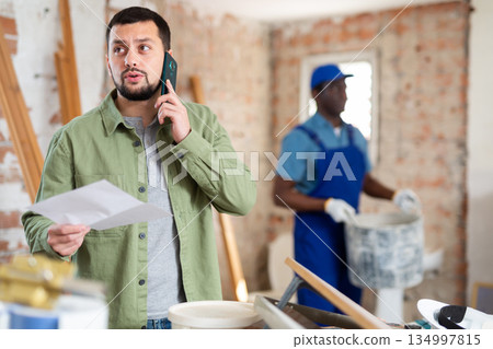 Engineer holds an estimate in his hands, talking on a mobile phone Engineer holds an estimate in his hands, talking on a mobile phone 134997815