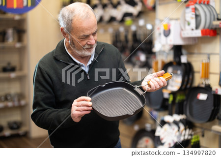 Elderly man chooses teflon-coated frying pan iron at supermarket 134997820