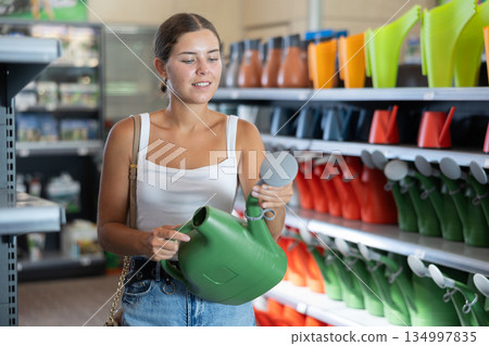 Young woman choosing watering can in store Young woman choosing watering can in store 134997835