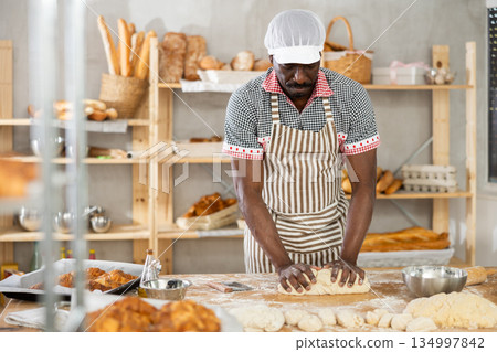 Professional African baker kneading dough on floured table Professional African baker kneading dough on floured table 134997842