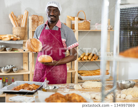 Male baker with basket of baked goods behind bakery counter inviting to buy bread Male baker with basket of baked goods behind bakery counter inviting to buy bread 134997869