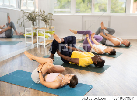 Young woman coach and students perform Supta kapotasana during training in studio Young woman coach and students perform Supta kapotasana during training in studio 134997897