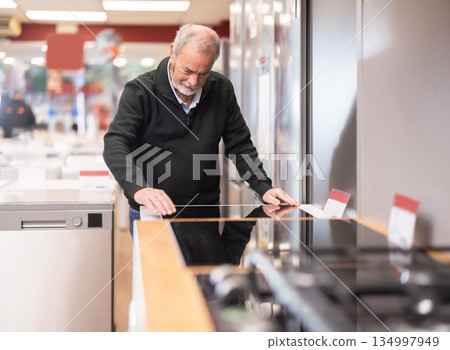 Senior man customer inspect product range and selects kitchen oven 134997949