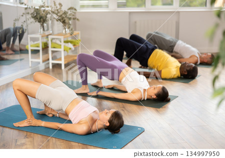 Young woman coach and students perform chatush padasana during training in studio Young woman coach and students perform chatush padasana during training in studio 134997950