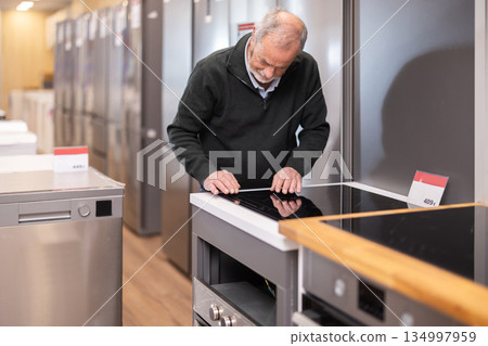 elderly man chooses a stove in a hardware store elderly man chooses a stove in a hardware store 134997959