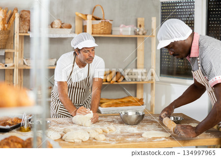 African man and male assistant make dough, employee kneads dough, assistant works with rolling pin 134997965