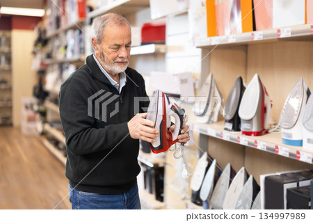 Elderly man chooses teflon-coated iron at supermarket Elderly man chooses teflon-coated iron at supermarket 134997989