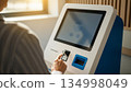 Senior woman using self service kiosk machine with touchscreen interface and card reader in modern indoor setting 134998049