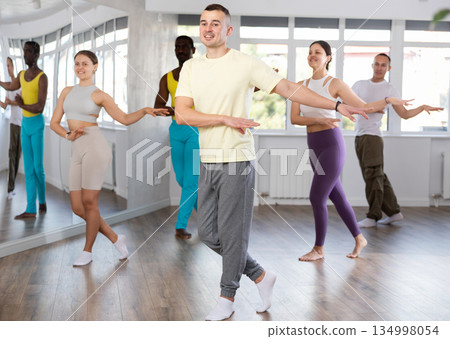 Positive dancing multiethnic active people enjoying social dance during group class in modern studio 134998054