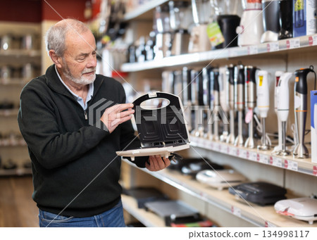 Elderly man chooses pancake maker at appliance store Elderly man chooses pancake maker at appliance store 134998117