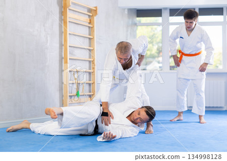 Judo or jiu jitsu classes - two men of different age practicing grabbing and throwing on sports mats Judo or jiu jitsu classes - two men of different age practicing grabbing and throwing on sports mats 134998128