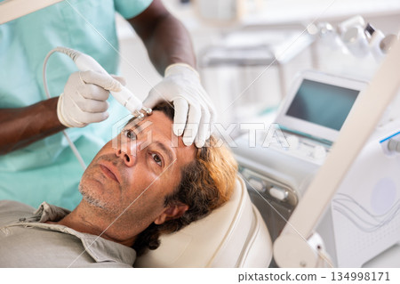 Middle-aged man receiving cosmetic facial radiofrequency procedure Middle-aged man receiving cosmetic facial radiofrequency procedure 134998171