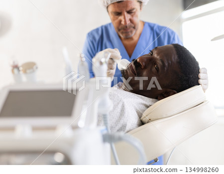 African man client undergoes facial skin care procedure using nozzle cold hammer whitening African man client undergoes facial skin care procedure using nozzle cold hammer whitening 134998260