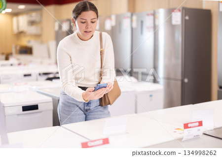 Woman scans a QR code on a washing machine logo to verify information at supermarket Woman scans a QR code on a washing machine logo to verify information at supermarket 134998262