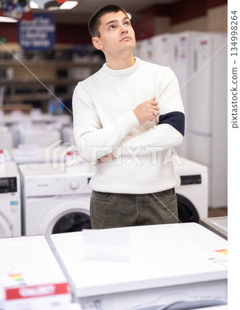 Young man customer inspect product range and selects dishwashing machine or washing machine Young man customer inspect product range and selects dishwashing machine or washing machine 134998264