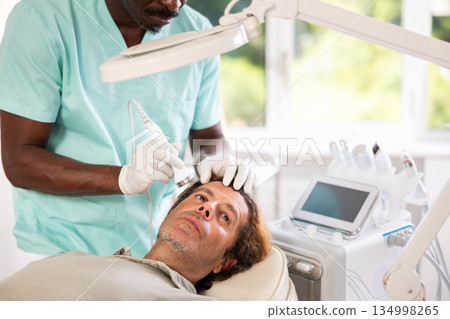 African male specialist uses ultrasonic import nozzle to care man client face skin African male specialist uses ultrasonic import nozzle to care man client face skin 134998265