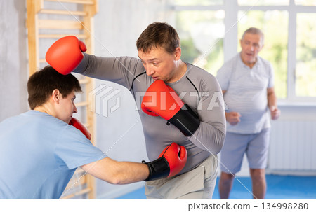 Man getting powerful blow to body during boxing sparring with young opponent Man getting powerful blow to body during boxing sparring with young opponent 134998280