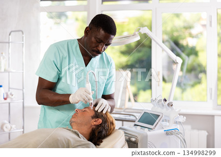 African American esthetician performing facial procedure with ion bubble attachment on man 134998299