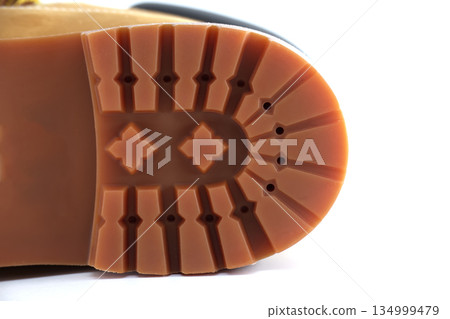 Close-up view of a rugged tan boot sole with deep treads and a distinctive pattern Close-up view of a rugged tan boot sole with deep treads and a distinctive pattern 134999479
