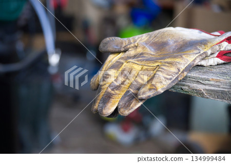 Dirty Work Gloves Resting On Weathered Wood Bench In A Busy Workshop During Construction Project Dirty Work Gloves Resting On Weathered Wood Bench In A Busy Workshop During Construction Project 134999484
