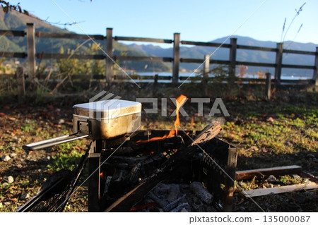 Autumn camping scene with people enjoying a bonfire and cooking rice in a mess kit on the shores of Lake Kawaguchi 135000087