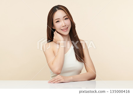 A beautiful young Asian woman with clean, fresh skin against a beige background. Skincare, facial treatment, cosmetology, beauty, and spa. An elegant portrait of an Asian woman. 135000416