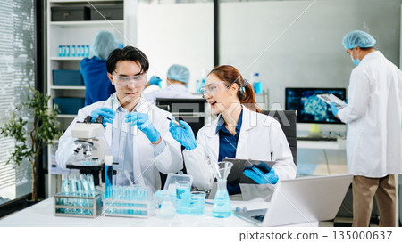 Team of scientists analyzing blue liquid samples in a modern lab, showcasing biotechnology, chemistry, and medical research innovation. Team of scientists analyzing blue liquid samples in a modern lab, showcasing biotechnology, chemistry, and medical research innovation. 135000637