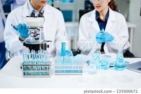 scientists in lab coats conducting research, handling glassware, and working with chemicals in a modern, high tech laboratory. 135000672