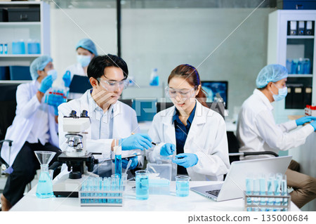 Team of scientists analyzing blue liquid samples in a modern lab, showcasing biotechnology, chemistry, and medical research innovation. 135000684