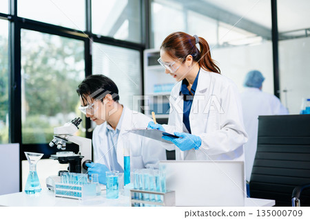 Scientists collaborating in a modern biotechnology lab with microscopes and test tubes, symbolizing teamwork, chemistry, and scientific innovation. 135000709
