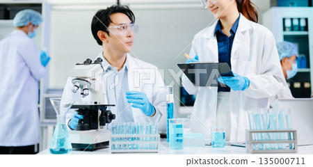 Scientists collaborating in a modern biotechnology lab with microscopes and test tubes, symbolizing teamwork, chemistry, and scientific innovation. 135000711