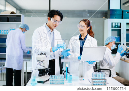 Scientists collaborating in a bright modern lab with blue liquids and microscopes, symbolizing teamwork, biotechnology, chemistry, and medical innovation. Scientists collaborating in a bright modern lab with blue liquids and microscopes, symbolizing teamwork, biotechnology, chemistry, and medical innovation. 135000734