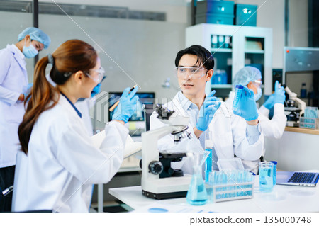 Professional scientists analyzing samples in a modern lab with blue liquids and microscopes, representing biotechnology, chemistry, and healthcare innovation. 135000748